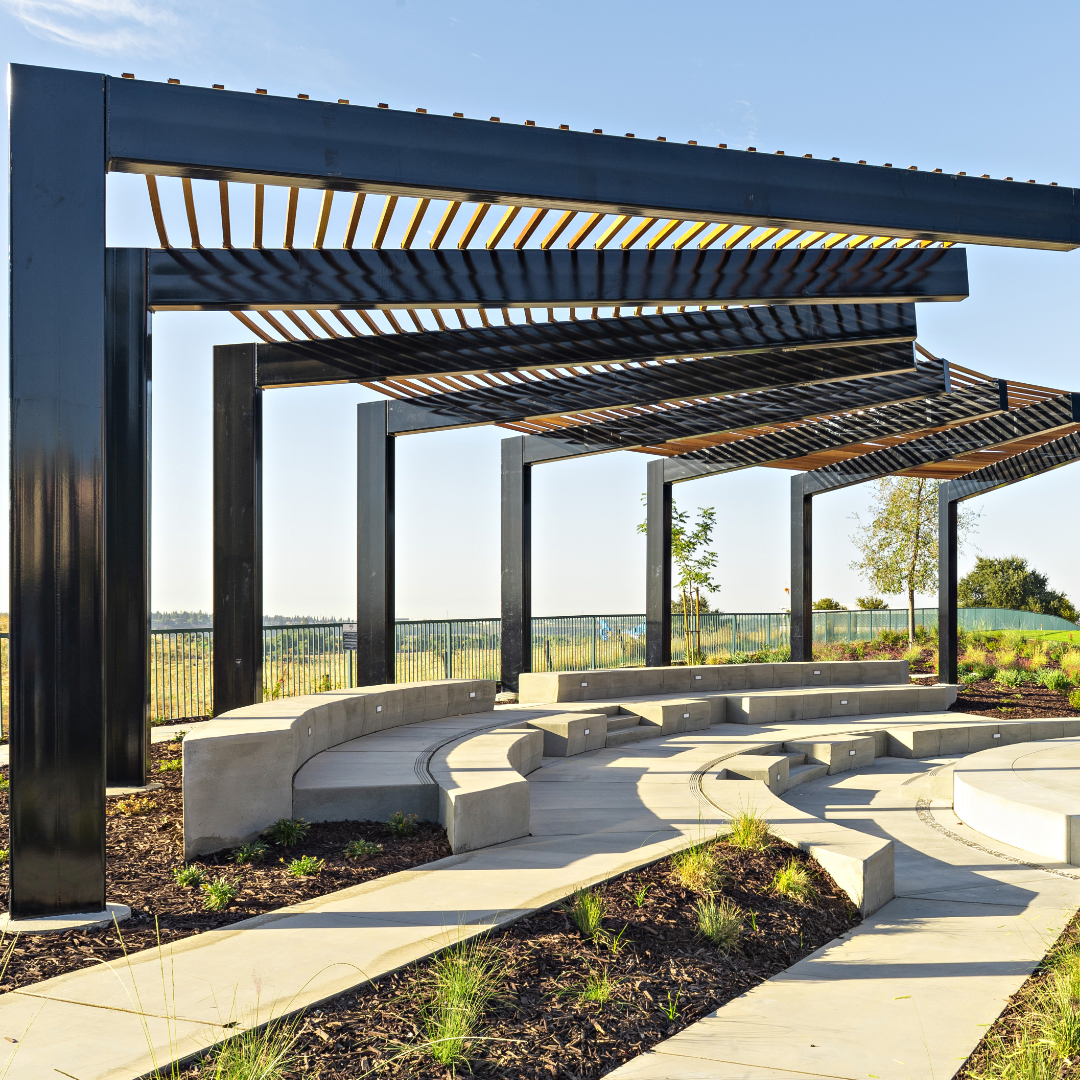 Large custom steel arbor structure with concrete amphitheater on a sunny day. 